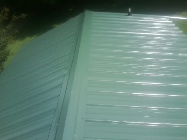 New green metal panels meeting at the ridge of a roof — Flat Roof Repair work by our crew in Hopewell