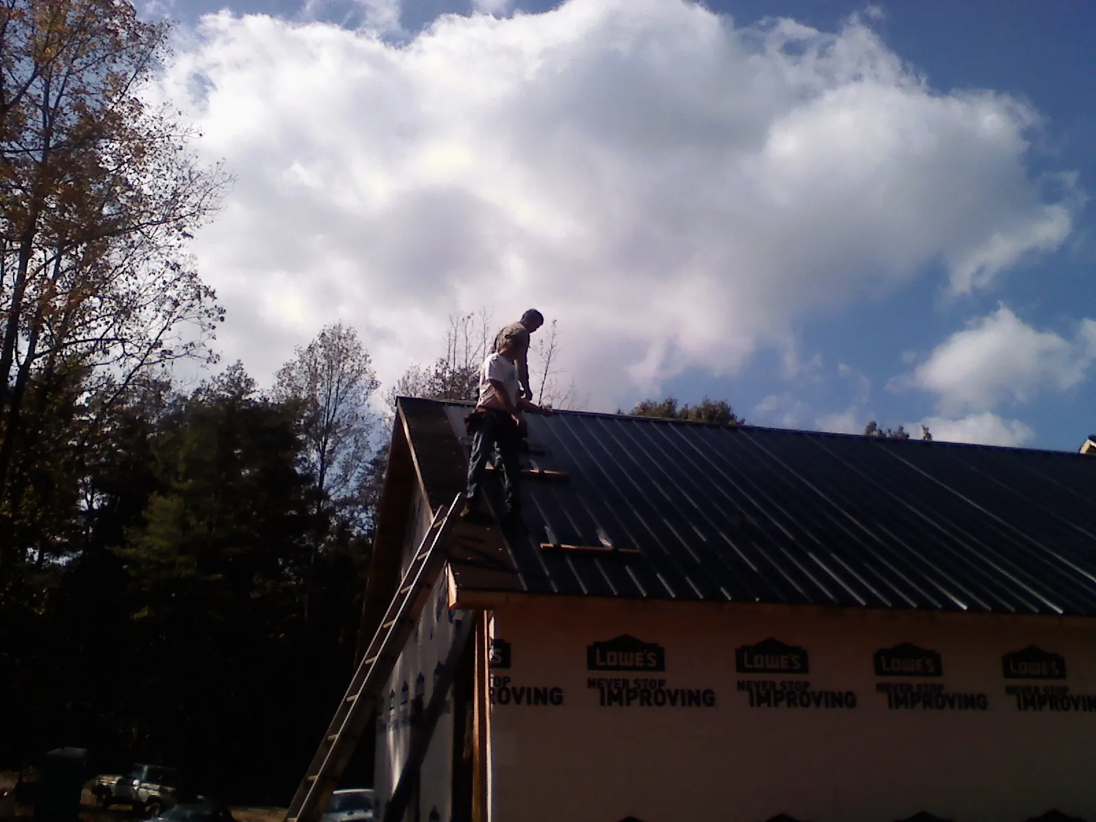 Roofer fastening dark metal panels high against a cloudy sky, from a Roof Inspection job in Hopewell