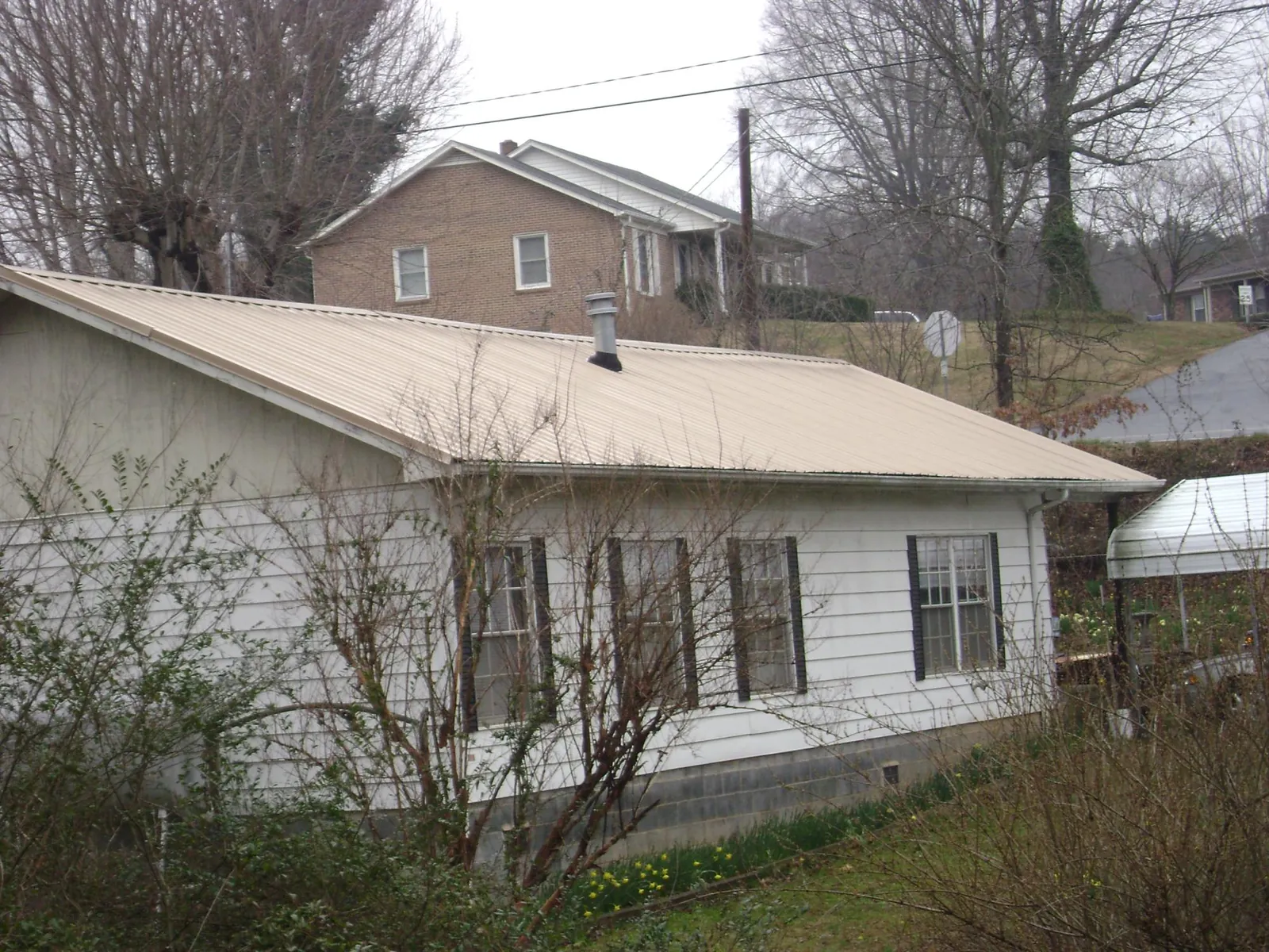 Tan metal roof on a white sided house set into a hillside — Commercial Roofing by Roofing Brothers in Hopewell